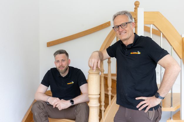 Markus Kaymer sitzt links auf einer Treppe. Rechts neben der Treppe steht Klaus Herold.